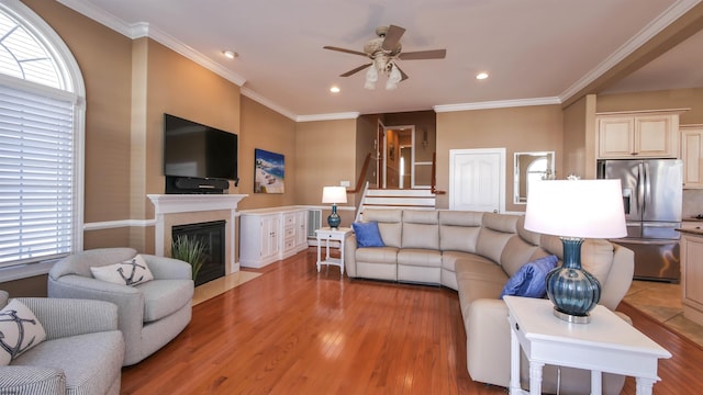 living area featuring a fireplace with flush hearth, light wood-style flooring, and crown molding