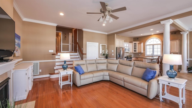 living area featuring a fireplace with flush hearth, visible vents, decorative columns, and light wood-style flooring