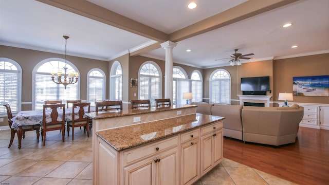 kitchen with ceiling fan with notable chandelier, ornamental molding, a center island, and ornate columns