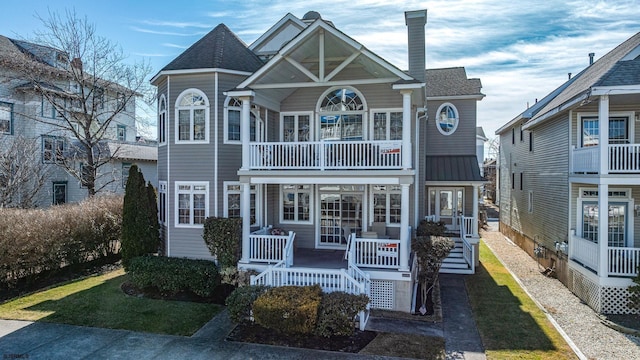 view of front of home featuring a porch, a shingled roof, a chimney, and a balcony