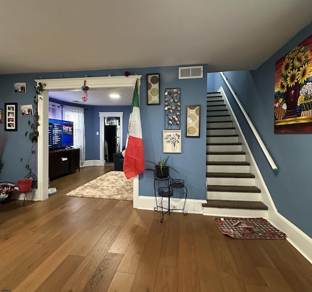 living area with stairs, visible vents, baseboards, and wood finished floors