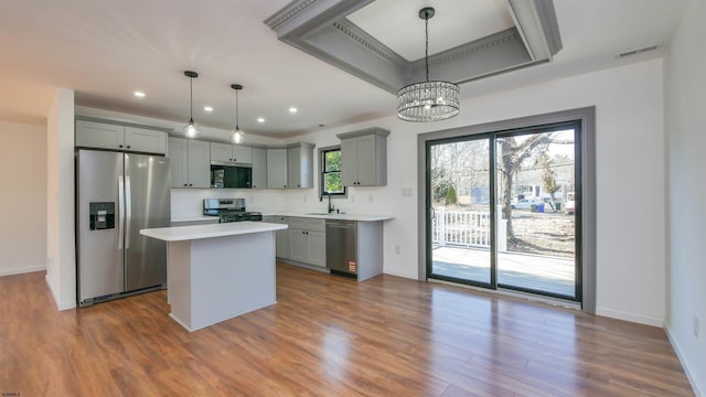 kitchen featuring a raised ceiling, light countertops, gray cabinets, appliances with stainless steel finishes, and a sink