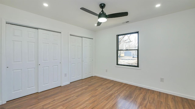 unfurnished bedroom featuring baseboards, visible vents, wood finished floors, multiple closets, and recessed lighting