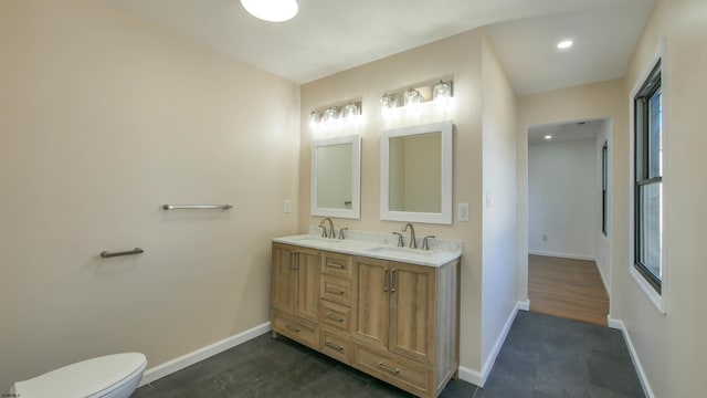 bathroom featuring toilet, double vanity, baseboards, and a sink