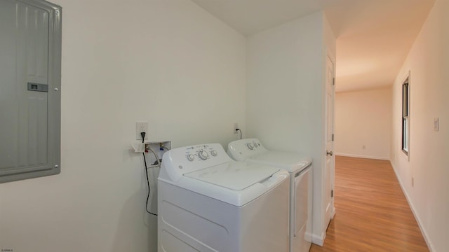 clothes washing area with laundry area, electric panel, baseboards, washer and dryer, and light wood-type flooring