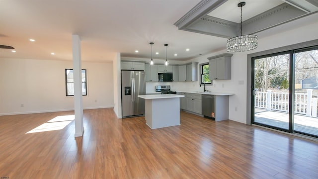 kitchen with gray cabinetry, stainless steel appliances, a sink, open floor plan, and light countertops