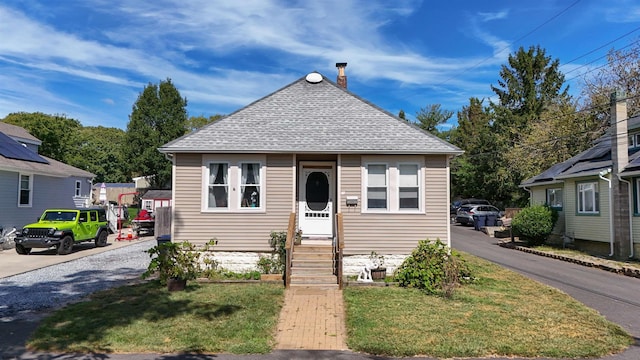 bungalow-style house with a front yard, roof with shingles, and a chimney