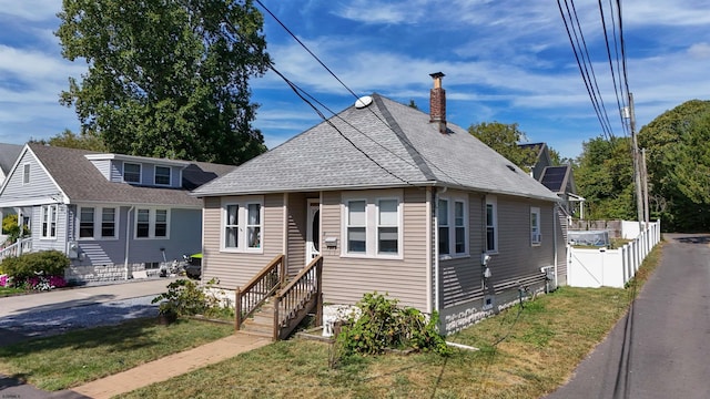 bungalow with a shingled roof, fence, entry steps, a front yard, and a chimney