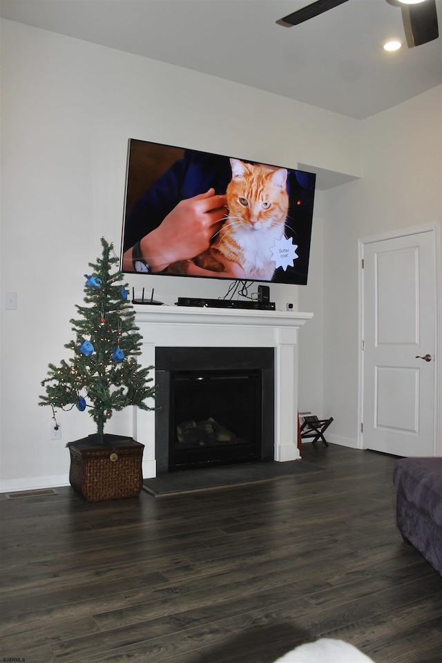 living area featuring wood finished floors, a fireplace with raised hearth, baseboards, and ceiling fan