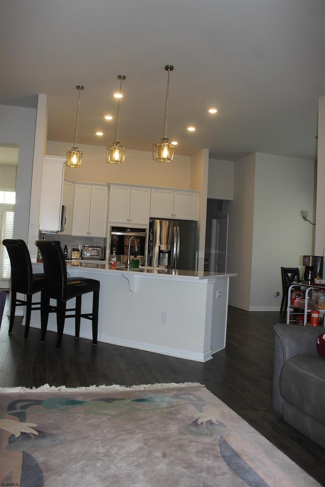 kitchen with a peninsula, stainless steel fridge with ice dispenser, dark wood-style flooring, white cabinets, and a kitchen breakfast bar