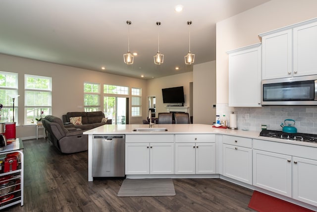 kitchen with a peninsula, a sink, decorative backsplash, stainless steel appliances, and open floor plan