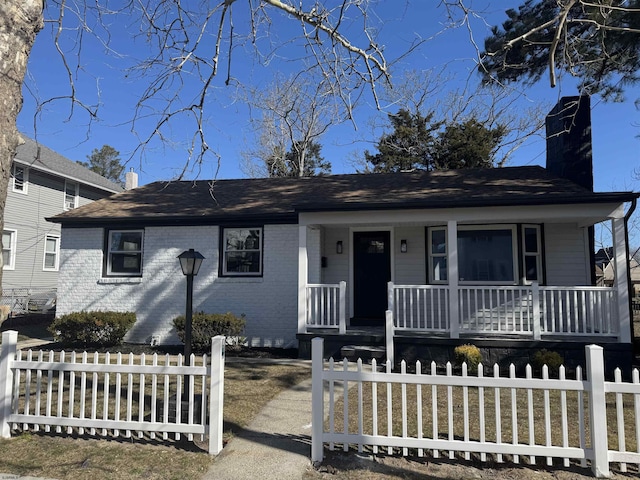 view of front of house with a porch, brick siding, a fenced front yard, and a chimney