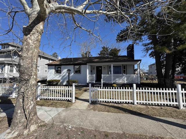 view of front of house featuring a fenced front yard, a porch, a chimney, and brick siding