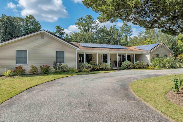 single story home featuring solar panels, aphalt driveway, covered porch, and a front lawn