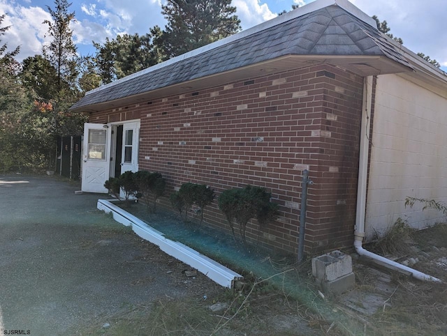 view of side of home with mansard roof, brick siding, and a shingled roof