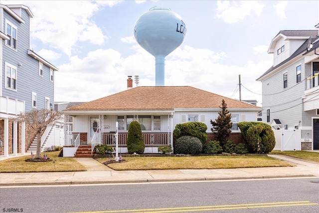 view of front of house with roof with shingles, covered porch, a chimney, a front lawn, and brick siding