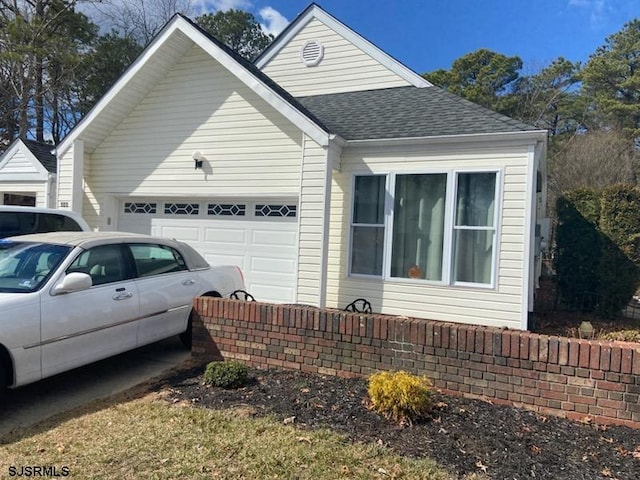 view of side of home featuring an attached garage and a shingled roof