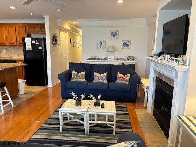 living area with recessed lighting, light wood-style flooring, ornamental molding, and a tile fireplace