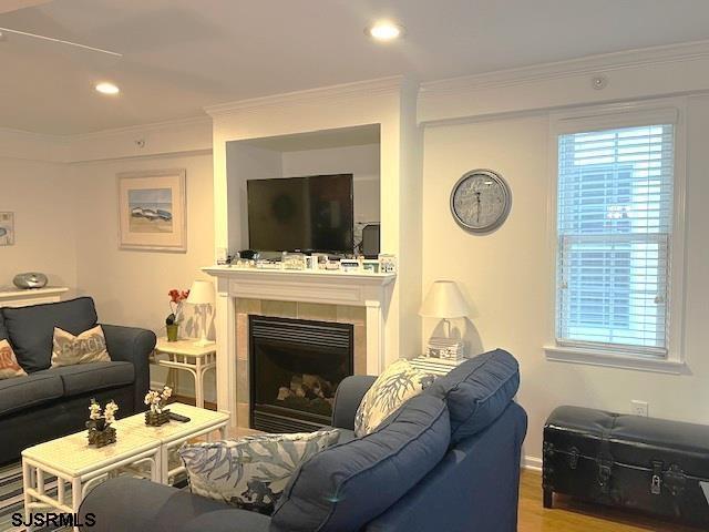 living area with recessed lighting, wood finished floors, ornamental molding, and a tiled fireplace