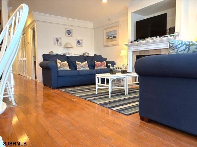 living room featuring a tiled fireplace, recessed lighting, crown molding, and hardwood / wood-style flooring