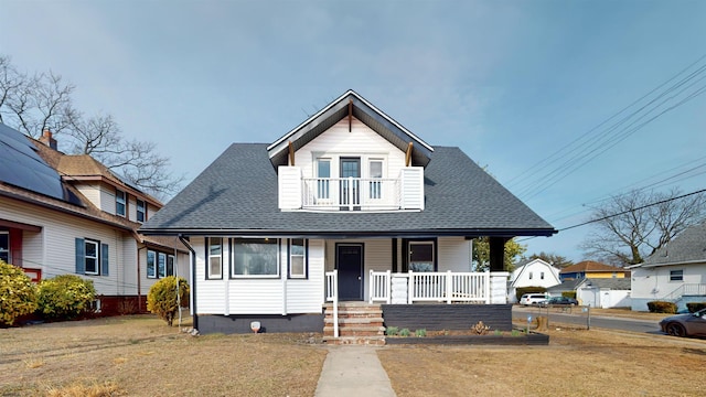 bungalow-style house with a balcony, covered porch, a front lawn, and a shingled roof