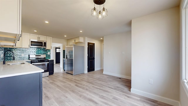 kitchen with light wood-style flooring, a sink, light countertops, appliances with stainless steel finishes, and tasteful backsplash