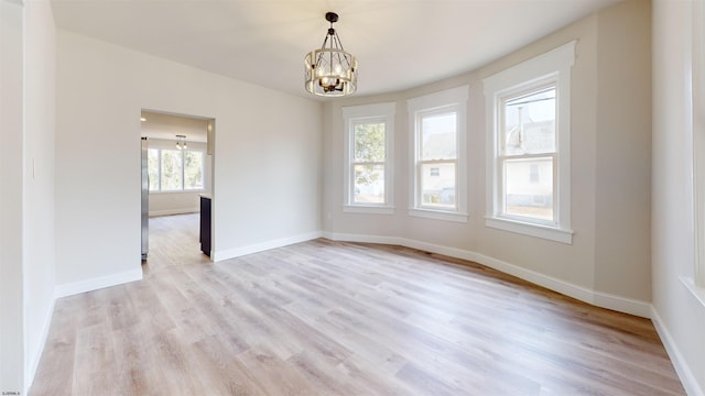 empty room with an inviting chandelier, baseboards, and light wood-type flooring