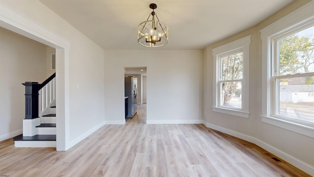 empty room featuring a wealth of natural light, baseboards, stairs, and light wood-style floors