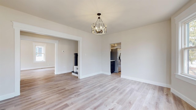 spare room with an inviting chandelier, plenty of natural light, light wood-style floors, and baseboards