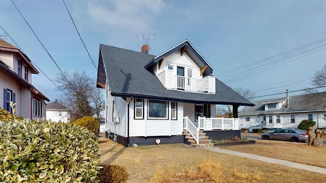 bungalow-style house with a shingled roof, a front lawn, a porch, a chimney, and a balcony