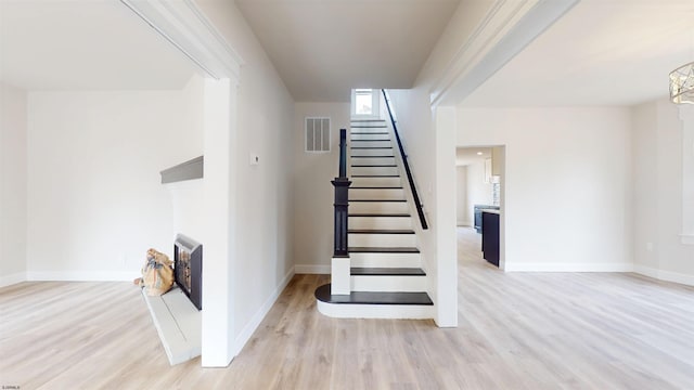 staircase featuring visible vents, baseboards, wood finished floors, and a fireplace