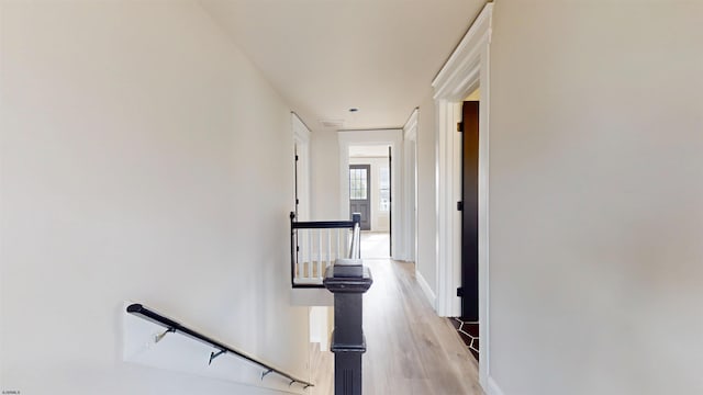 hallway featuring light wood-type flooring, an upstairs landing, and baseboards