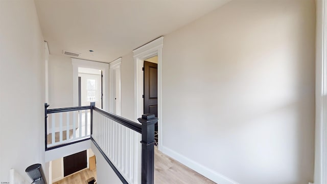 corridor with baseboards, an upstairs landing, visible vents, and light wood finished floors