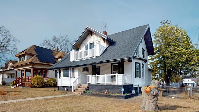 view of front facade featuring a front lawn, roof with shingles, covered porch, a chimney, and a balcony