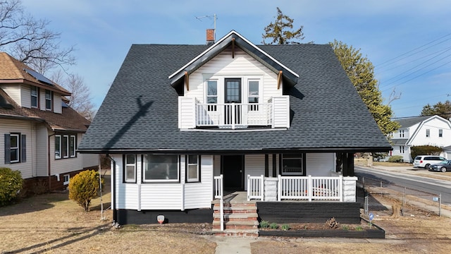 view of front facade with a balcony, a porch, a chimney, and roof with shingles