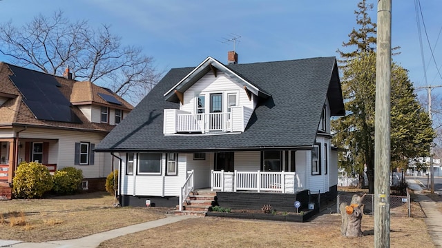 view of front of property featuring a balcony, covered porch, a chimney, and a shingled roof