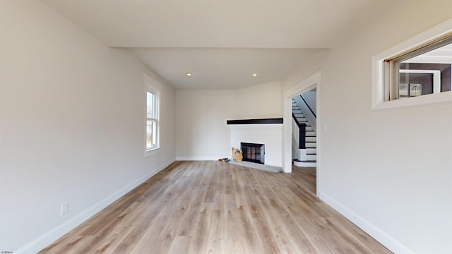 unfurnished living room featuring wood finished floors, baseboards, a glass covered fireplace, and stairs