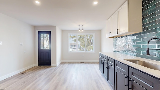 kitchen with a sink, baseboards, backsplash, and light wood-style flooring