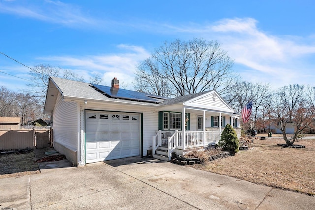 ranch-style house featuring driveway, covered porch, an attached garage, solar panels, and a chimney