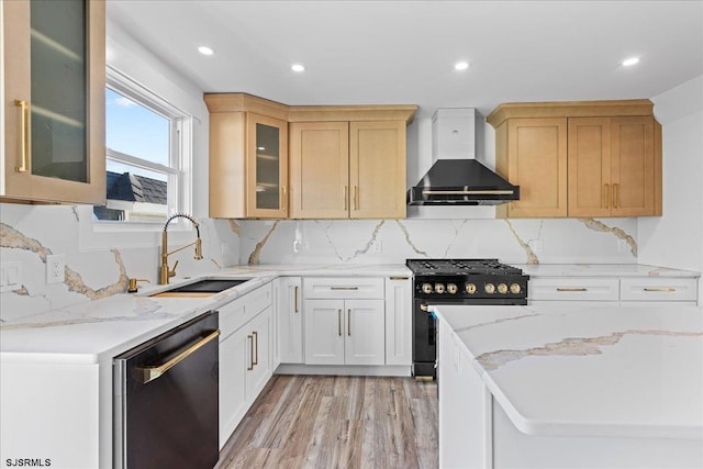 kitchen with a sink, wall chimney range hood, gas stove, light wood finished floors, and dishwashing machine