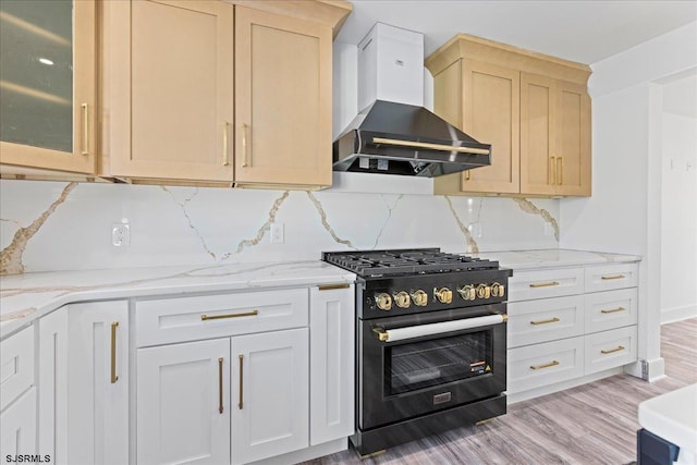 kitchen featuring tasteful backsplash, wall chimney range hood, light brown cabinetry, light stone counters, and stainless steel stove