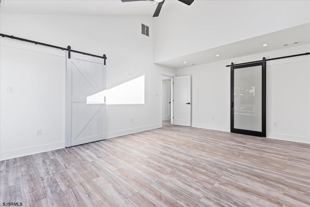 empty room with visible vents, light wood-style flooring, a ceiling fan, a barn door, and baseboards