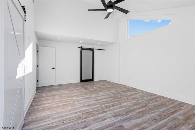 unfurnished room featuring a barn door, light wood finished floors, and ceiling fan