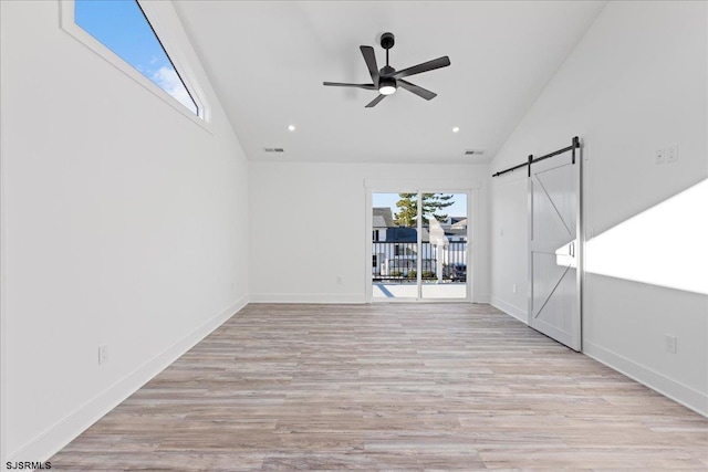 unfurnished room featuring a barn door, a healthy amount of sunlight, wood finished floors, and visible vents