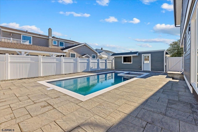 view of swimming pool with a patio area, a pool with connected hot tub, an outbuilding, and a fenced backyard