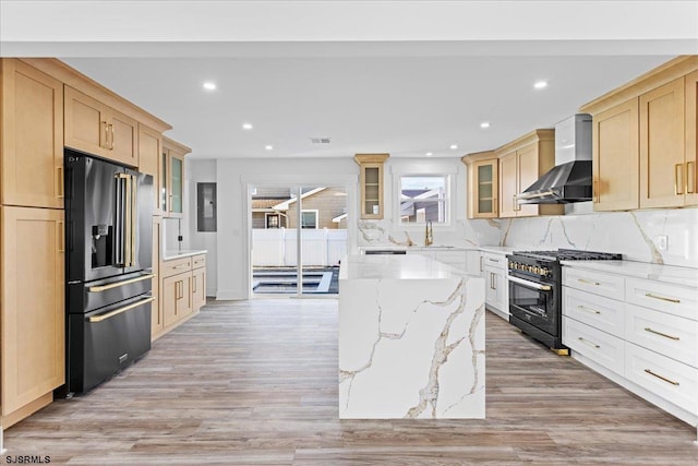 kitchen with glass insert cabinets, high end black range oven, wall chimney exhaust hood, and fridge with ice dispenser