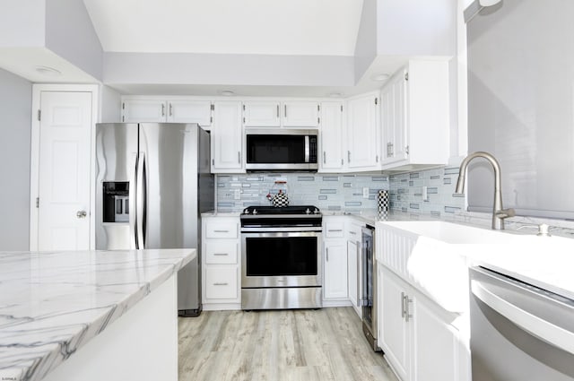 kitchen featuring light wood finished floors, white cabinets, backsplash, and appliances with stainless steel finishes