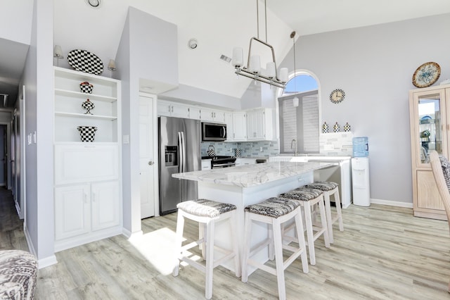 kitchen featuring a breakfast bar, backsplash, a kitchen island, stainless steel appliances, and light wood-style floors