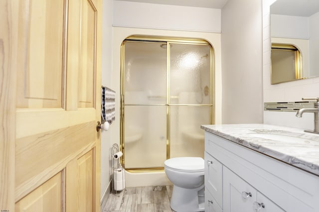 bathroom featuring vanity, wood finished floors, a shower stall, toilet, and tasteful backsplash