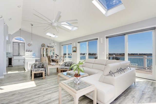 living area with light wood finished floors, a water view, wine cooler, a skylight, and high vaulted ceiling